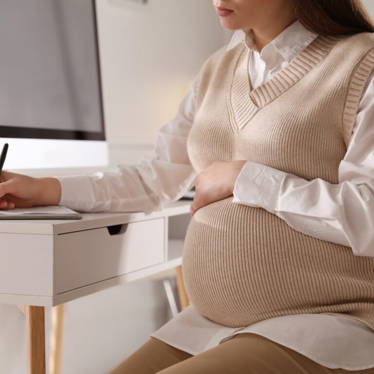 Pregnant woman working at a tables accessing support. This image depicts a supportive workplace experience for expecting mothers in 2024