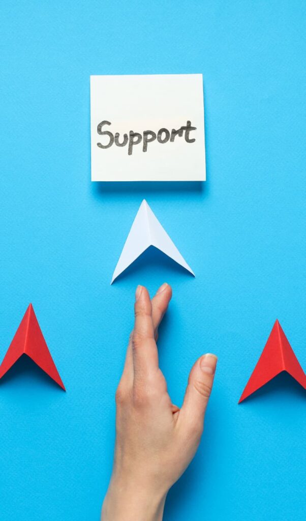 Hand pointing to a white sticky note with the word "Support" written in black marker.